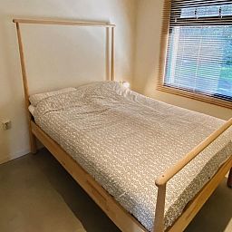 Terrasse des Ferienhauses DG357 in Meppen, Drenthe mit Holzstuehlen und gruener Umgebung.