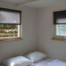 Gemuetliches Wohnzimmer im Ferienhaus DG280 in Exloo, Suedost-Drenthe, mit bequemem roten Sofa und Blick auf die gruene Natur.