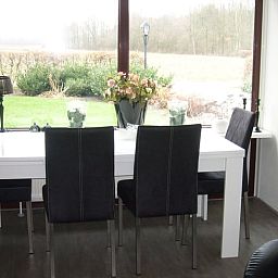 Gemuetlicher Essbereich im Ferienhaus in Valthe, Suedost-Drenthe, mit Blick auf die ruhige Natur durch grosse Fenster.