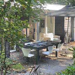 Gezellige terras van Vakantiehuisje in Doldersum, Zuidwest Drenthe, omgeven door groen en uitgerust met een ruime eettafel en parasol.