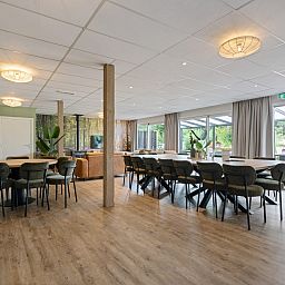 Ruime binnenruimte van Groepsaccommodatie de Komeet in Dwingeloo, Drenthe, met grote tafels en uitzicht op de groene omgeving.