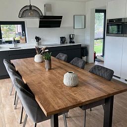 Stijlvolle eetruimte in Vakantiehuis Cube Elite 6, Biddinghuizen, Flevoland met grote houten tafel en moderne keuken.