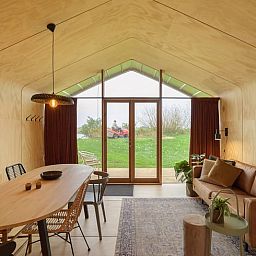 Gemuetliche Einrichtung des Ferienhauses in Broek in der friesischen Landschaft, mit Holzinterieur und Blick auf die gruene Umgebung.