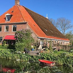 Zufahrtsstrasse zum Ferienhaus in Hegebeintum, umgeben von Baeumen und bunten Blumen in Friesland.