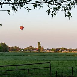 Blick auf die friesische Landschaft im Huisje in Echten, einem Ferienhaus in Friesland, mit einem Heissluftballon am heiteren Morgenhimmel.