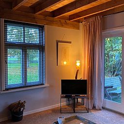 Gemuetliches Wohnzimmer des Ferienhauses in Laren, Achterhoek, Gelderland mit Blick auf den Garten und warmen Holzakzenten.