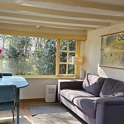 Gemuetliches Wohnzimmer des Ferienhauses in Harfsen, Achterhoek, Gelderland mit Blick in die Natur und bequemer Sitzecke.