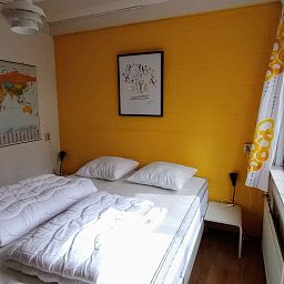 Sfeervolle slaapkamer in Huisje in Harfsen, vakantiehuis in Achterhoek, Gelderland met zonnige gele muur en comfortabel tweepersoonsbed.