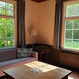 Cozy living room of Holiday Home in Vorden, Achterhoek, with large windows and views of the green nature of Gelderland.
