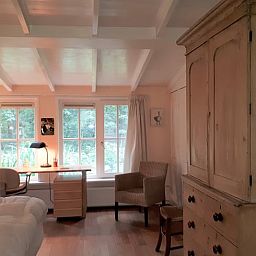 Gemuetliches Schlafzimmer im Ferienhaus in Joppe, Achterhoek, mit Holzmoebeln und Blick auf die gruene Natur durch grosse Fenster.