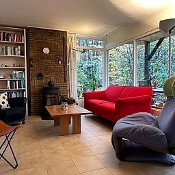Gemuetliches Wohnzimmer des Ferienhauses in Emst, gelegen in Veluwe, Gelderland, mit bequemen Sitzgelegenheiten und Blick auf die Natur.