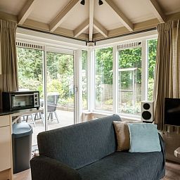 Cozy living room of a cottage in Ermelo, Veluwe, Gelderland, with a view of the green garden and modern amenities.