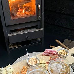 Cozy interior of Cottage in Epe, Veluwe with warm wood stove and drinks board, perfect for relaxation in Gelderland.