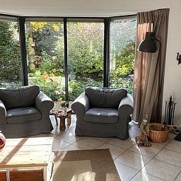 Gezellige woonkamer van Huisje in Epe, Veluwe, met comfortabele stoelen en uitzicht op de groene tuin, ideaal voor ontspanning.