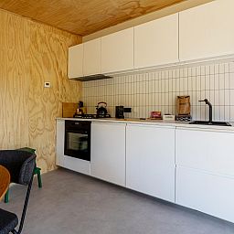 Moderne keuken in vakantiehuis Mos, Nunspeet, Veluwe met strakke witte kasten en houten accenten voor een gezellige sfeer.