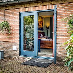 Charmanter Eingang zum Studio REE, Bed and Breakfast in Wekerom, Veluwe mit Gruenpflanzen und Backsteinmauer.