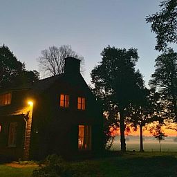 Stimmungsvoll beleuchtetes Landhaus in Geijsteren, Nord-Limburg, umgeben von Baeumen bei Sonnenuntergang.