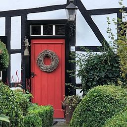 Red front door of Holiday home in Epen, South Limburg, surrounded by green bushes.