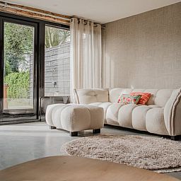 Gemuetliches Wohnzimmer im Ferienhaus in Leende, Nordbrabant mit bequemem Sofa und Gartenblick. Perfekt zum Entspannen.