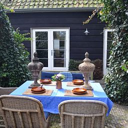 Gezellig terras bij Vakantiehuisje in Sleeuwijk, Noord Brabant, met rustieke eettafel en comfortabele stoelen omringd door groene natuur.