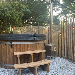 Rustieke hot tub in de tuin van Vakantiehuis in Overloon, omringd door groene natuur voor ultieme ontspanning.