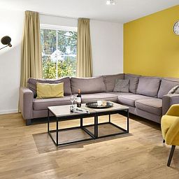 Comfortabele zithoek in De Vers 6-persoons bungalow 6C2, Overloon, met gele accenten en ruime bank.