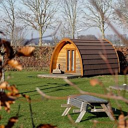 Rustikale Holzhuetten im Cottage in Terheijden, Westbrabant, umgeben von gruener Natur und Picknicktischen.