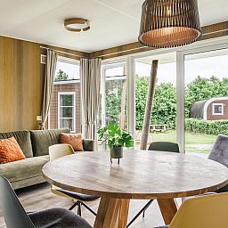 Gezellige woonkamer in Strandhuisje voor 5 personen, Julianadorp, Noordzeekust, met uitzicht op groene tuin en comfortabele zithoek.