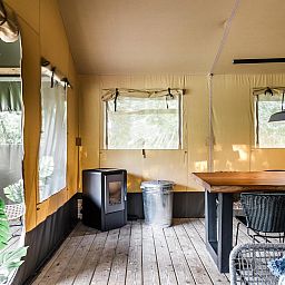 Binnenruimte van Strandtent 8 personen in Julianadorp, Noordzeekust. Gezellige glamping lodge met houten vloer en lichtinval door ramen.