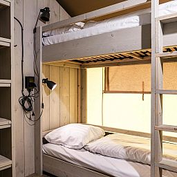 Gezellige slaapkamer in Strandtent 8 personen, een tenthuis in Julianadorp aan de Noordzeekust, Noord-Holland, met stapelbedden en houten interieur.
