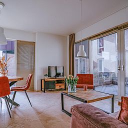 Gemuetliches Wohnzimmer des Ferienhauses Zeebaars in Egmond aan Zee, Nordholland, mit Blick auf die Terrasse an der Nordseekueste.