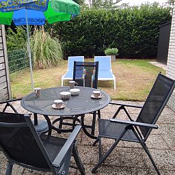 Terrasse des NH549 in Callantsoog, Nordseekueste, mit Gartenmoebeln und gruenem Garten zum Entspannen im Freien.