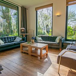 Gezellige woonkamer van Landhuis Duinzicht in Callantsoog, Noord-Holland met uitzicht op de groene tuin aan de Noordzeekust.