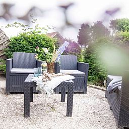 Sonnige Terrasse am Ferienhaus in Callantsoog, Nordseekueste, Nordholland, mit bequemen Sitzgelegenheiten.