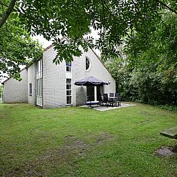 Terras van vakantiehuis in Julianadorp aan Zee met tuinmeubilair en parasol.