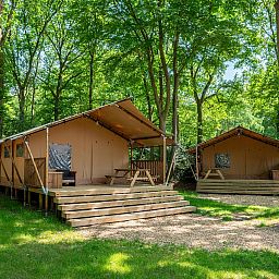 De Bos Escape glamping lodge in Huizen, Noord-Holland, omgeven door groene natuur en voorzien van een ruime veranda voor een ontspannen verblijf.