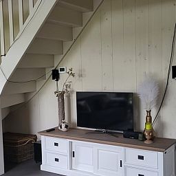 Gemuetliches Wohnzimmer des Ferienhauses in Winkel, Nordholland, mit moderner Einrichtung und Treppe zum Obergeschoss, ideales Feriendomizil.