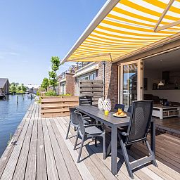 Enjoy the sunny terrace of Apartment Assum I in Uitgeest, North Holland, with views of the water and comfortable outdoor seating.