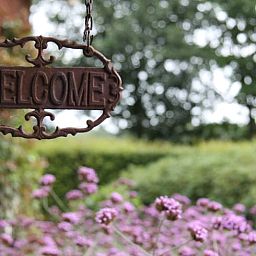 Willkommensschild am Eingang des Ferienhauses in Mander, Twente, Overijssel, umgeben von schoenen Blumen und Gruenanlagen.