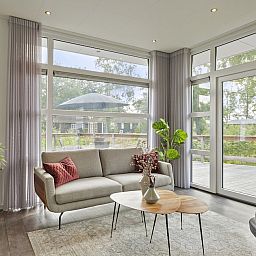 Helles Wohnzimmer im Ferienhaus Regge 4, Hoge Hexel, Twente mit Blick auf die Terrasse und die gruene Umgebung.