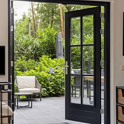 Gemuetlicher Innenbereich des Huisje in Holten mit Fluegeltueren zu einer sonnigen Terrasse, gelegen im gruenen Salland, Overijssel.