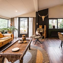 Geraeumiger Wohnraum im Ferienhaus in Rheezerveen, Vechtstreek, Overijssel mit Holzboeden und einer gemuetlichen Sitzecke.