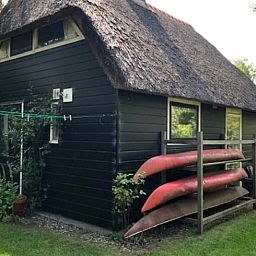 Rustikales Ferienhaus in Giethoorn, gelegen im malerischen Nordwesten von Overijssel, umgeben von Gruen und mit einem Reetdach.