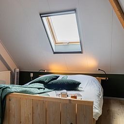 Sfeervolle slaapkamer in Vakantiehuisje in Wetering, Overijssel. Comfortabel bed onder een dakraam.