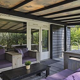 Entspannen Sie sich auf der ueberdachten Veranda des Bungalows Schoonoord in Doorn, Utrechtse Heuvelrug, mit Blick auf die gruene Umgebung.