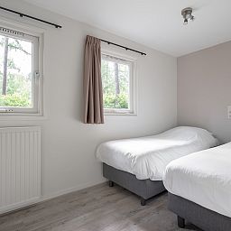 Schlafzimmer im Bungalow Schoonoord, Doorn, Utrechtse Heuvelrug, mit zwei bequemen Betten und Blick auf die gruene Natur.