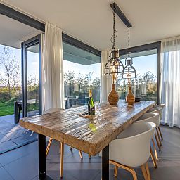 Ruime eetruimte in Duinvallei 39, De Groote Duynen, Kamperland, met moderne stoelen en een glazen wand.