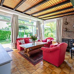 Gemuetliches Wohnzimmer in der Leeuwerikenlaan 15, De Banjaard, Kamperland mit grossen Fenstern und bequemen roten Sofas.