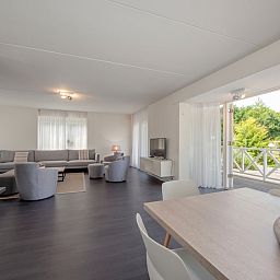Geraeumiges Wohnzimmer der Villa R10B in Kamperland, Noord-Beveland, Zeeland mit moderner Einrichtung und Blick auf die gruene Umgebung.