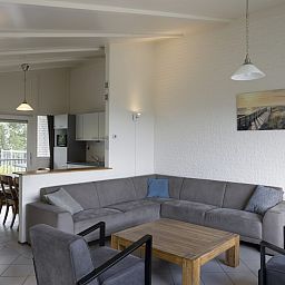 Gemuetliches Wohnzimmer im Bungalow BE, Kamperland, Noord-Beveland, Zeeland mit geraeumiger Sitzecke und Blick auf die gruene Umgebung.